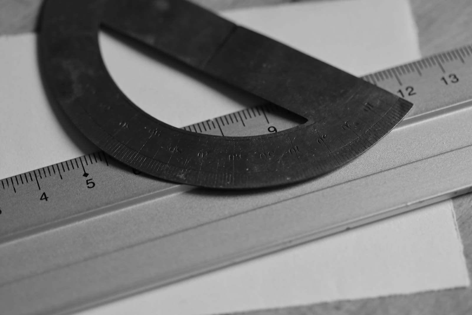 A black protractor resting on a steel rule over a drawing